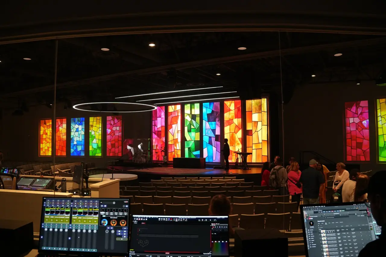 Front-of-house lighting console and screens facing a stage lit with multicolor LED columns