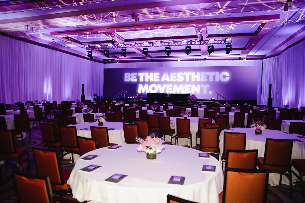 Ballroom with round tables and an LED wall reading BE THE AESTHETIC MOVEMENT