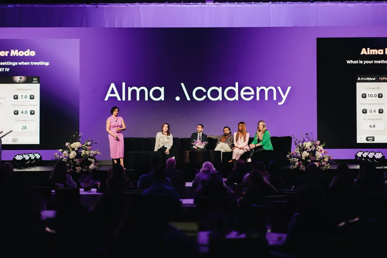Panel discussion on stage between two Alma Academy LED screens