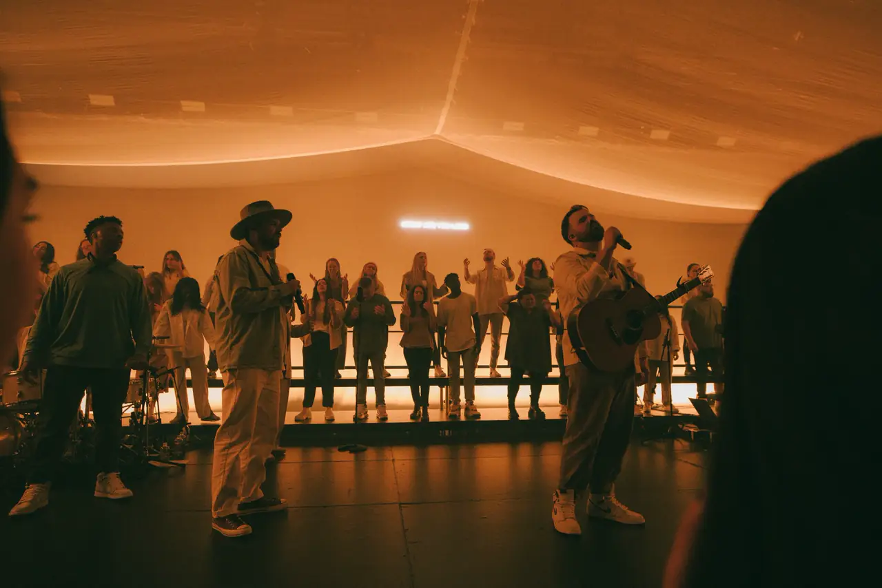 Singers on stage in amber light under a curved ceiling