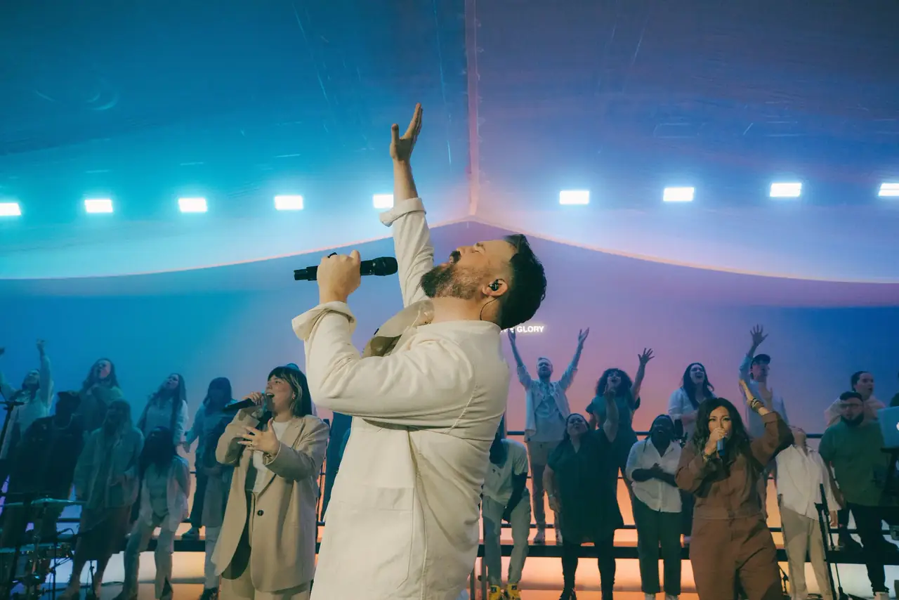 Firm Foundation: Cody Carnes in white under cyan light, the choir behind him