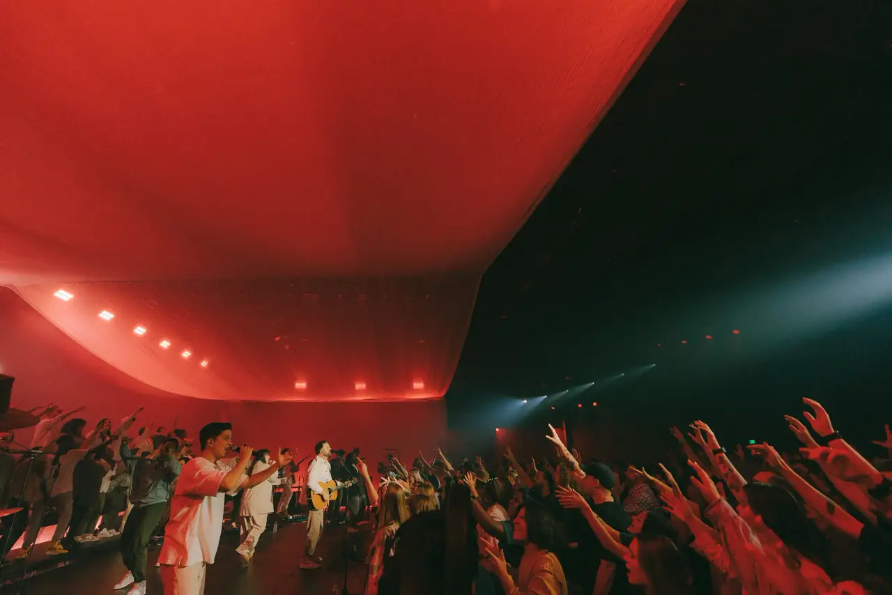 Firm Foundation recording: a room washed in red light with hands raised toward the stage
