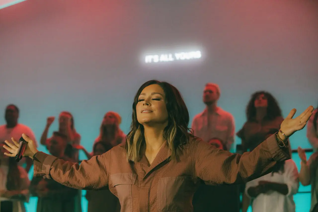 Singer with arms open in front of a teal-lit wall during the recording