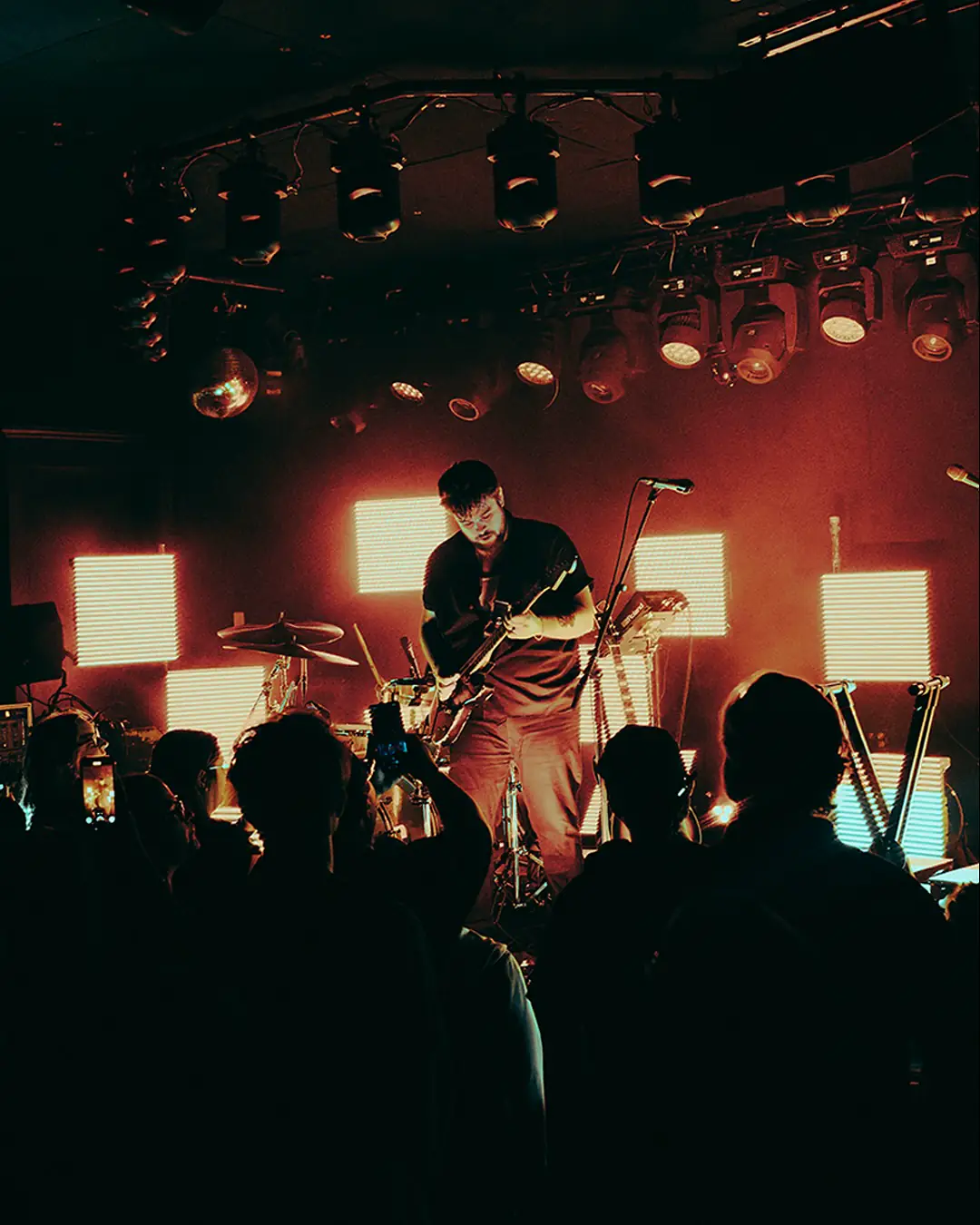 Stephen Stanley playing guitar under warm stage light, square LED panels behind him and the crowd in silhouette