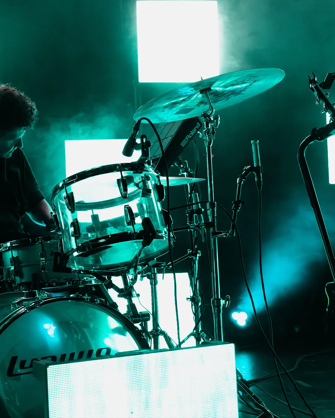 Drummer in teal light with square LED panels glowing behind the kit