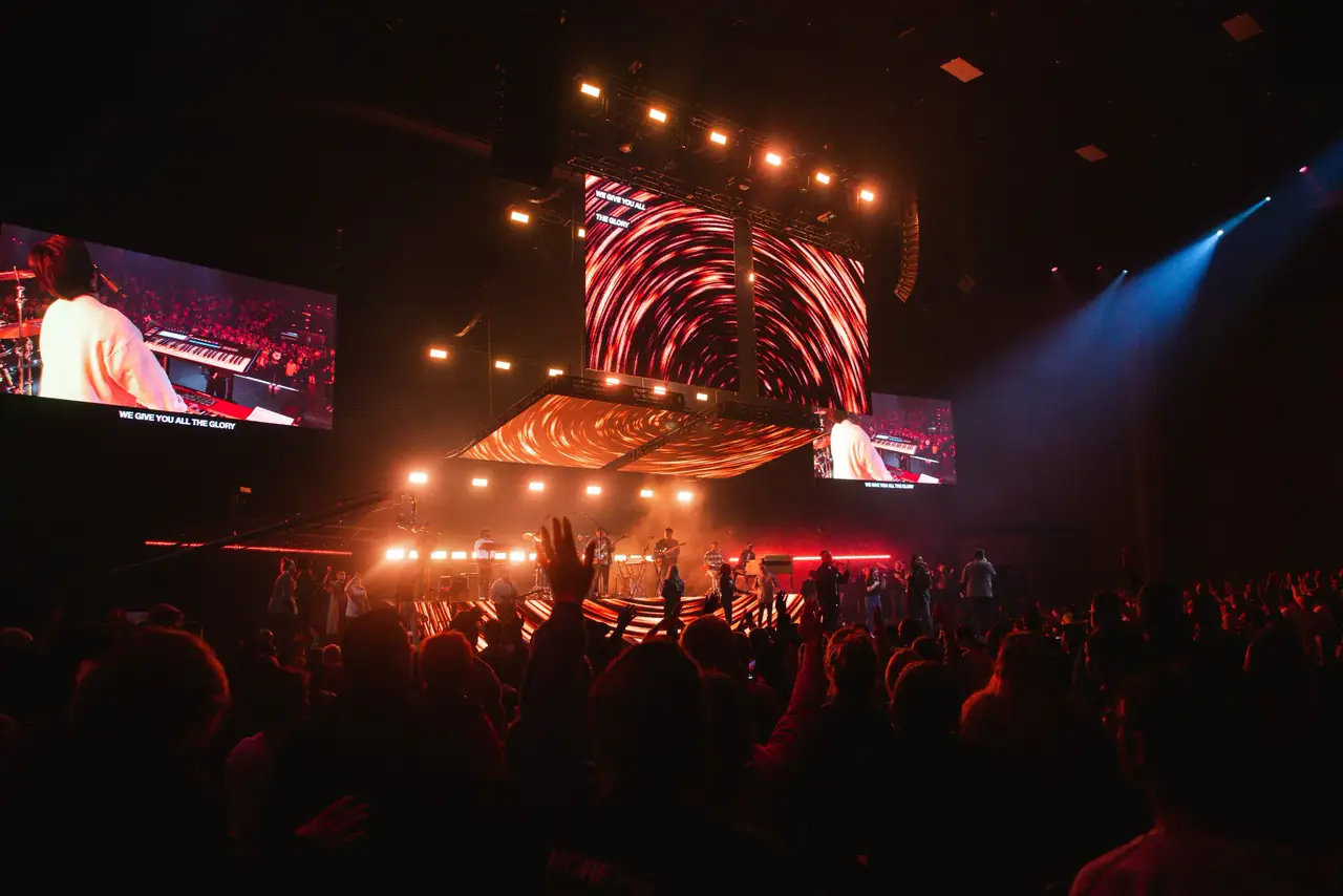 Crowd with hands raised facing an LED wall and warm stage lighting